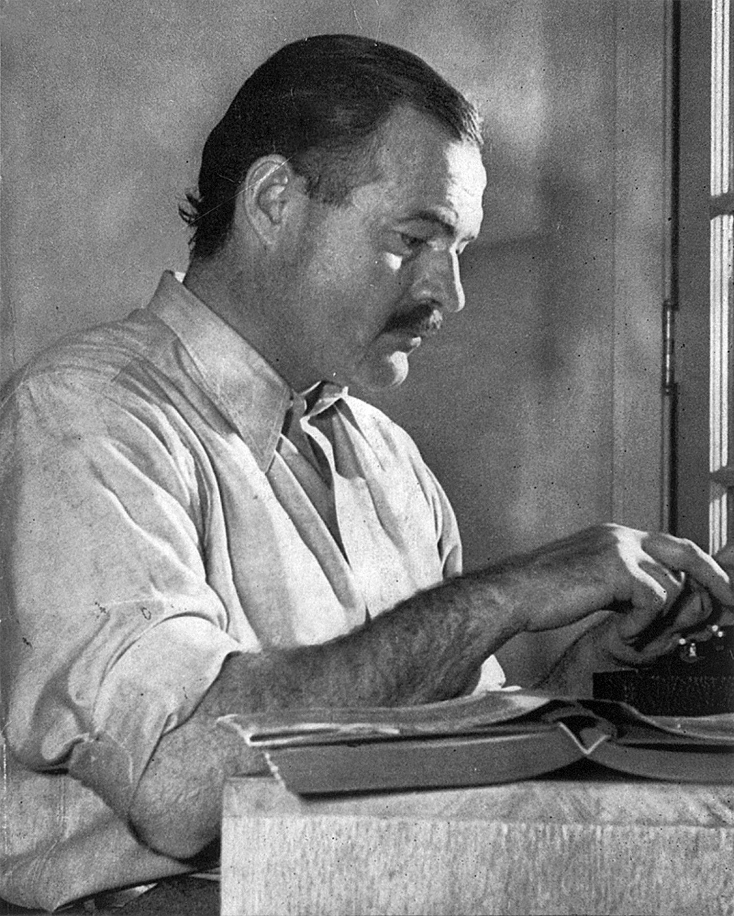 Ernest Hemingway writing at his desk.